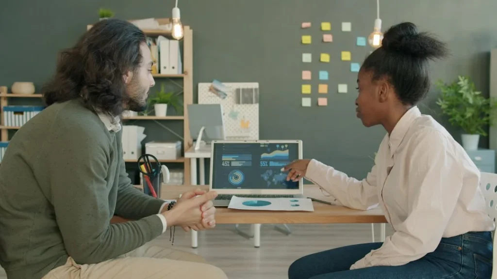Two colleagues discussing data on a laptop screen